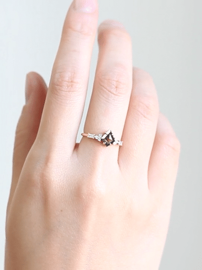 GIF of hand wearing petite ring with kite salt and pepper diamond, trefoil melee accents on shoulders, and baguette stones on band.