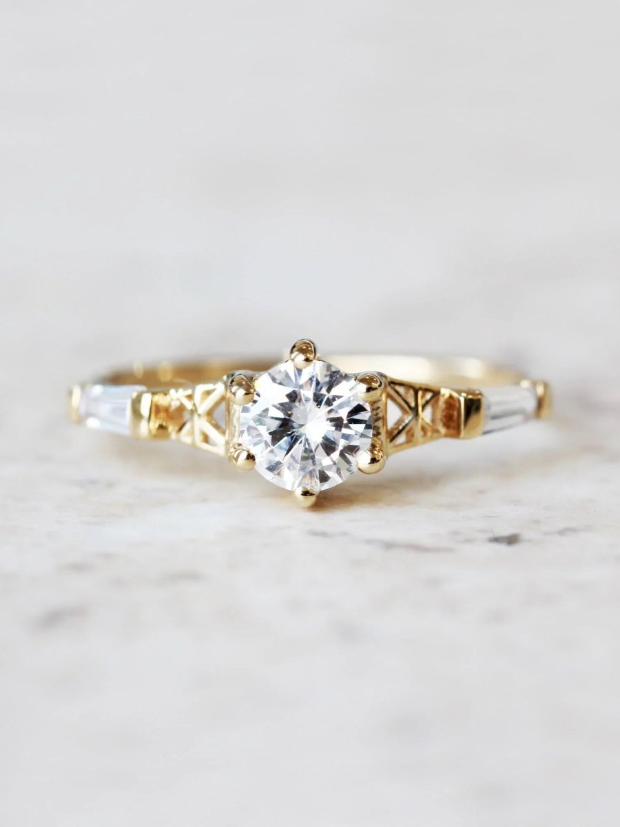 Face of round white diamond ring with gold flared latticed shank, Art Deco design elements, displayed on white marble