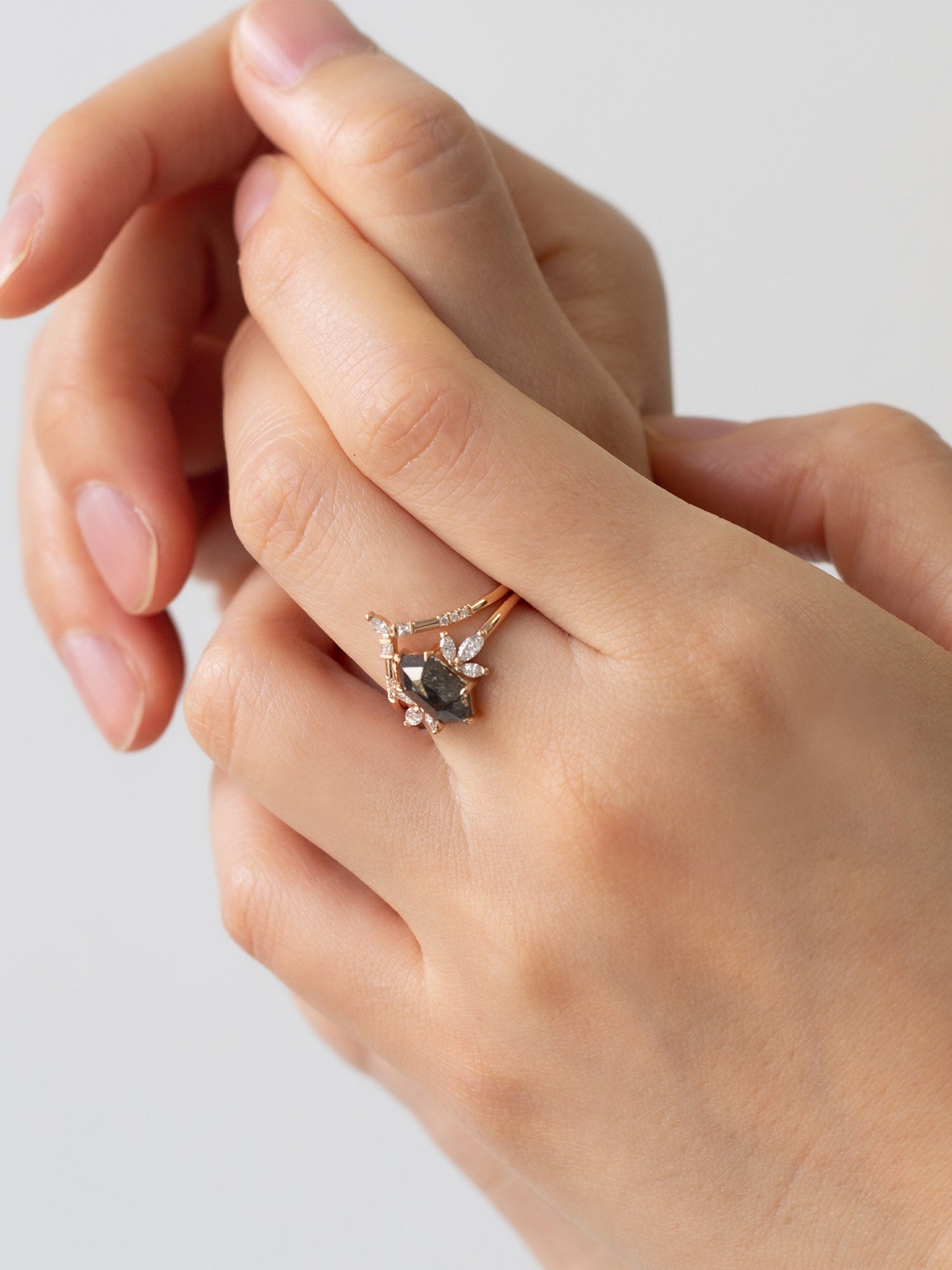 Art deco minimalistic hexagon salt and pepper diamond engagement ring in 14k rose gold with six smaller marquise diamonds with matching band on model's hand.