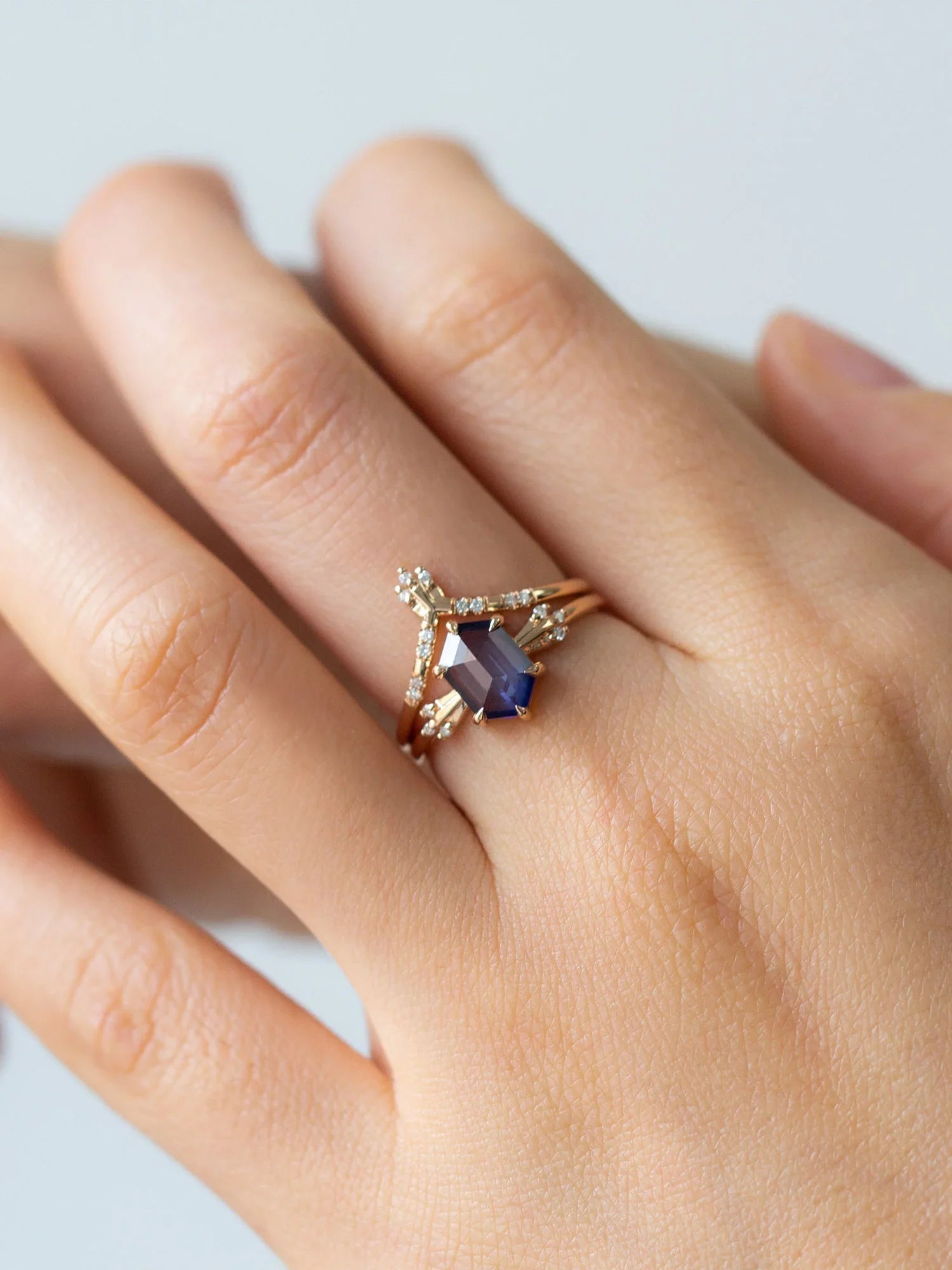 Hand wearing a ring with a blue gemstone on a light background