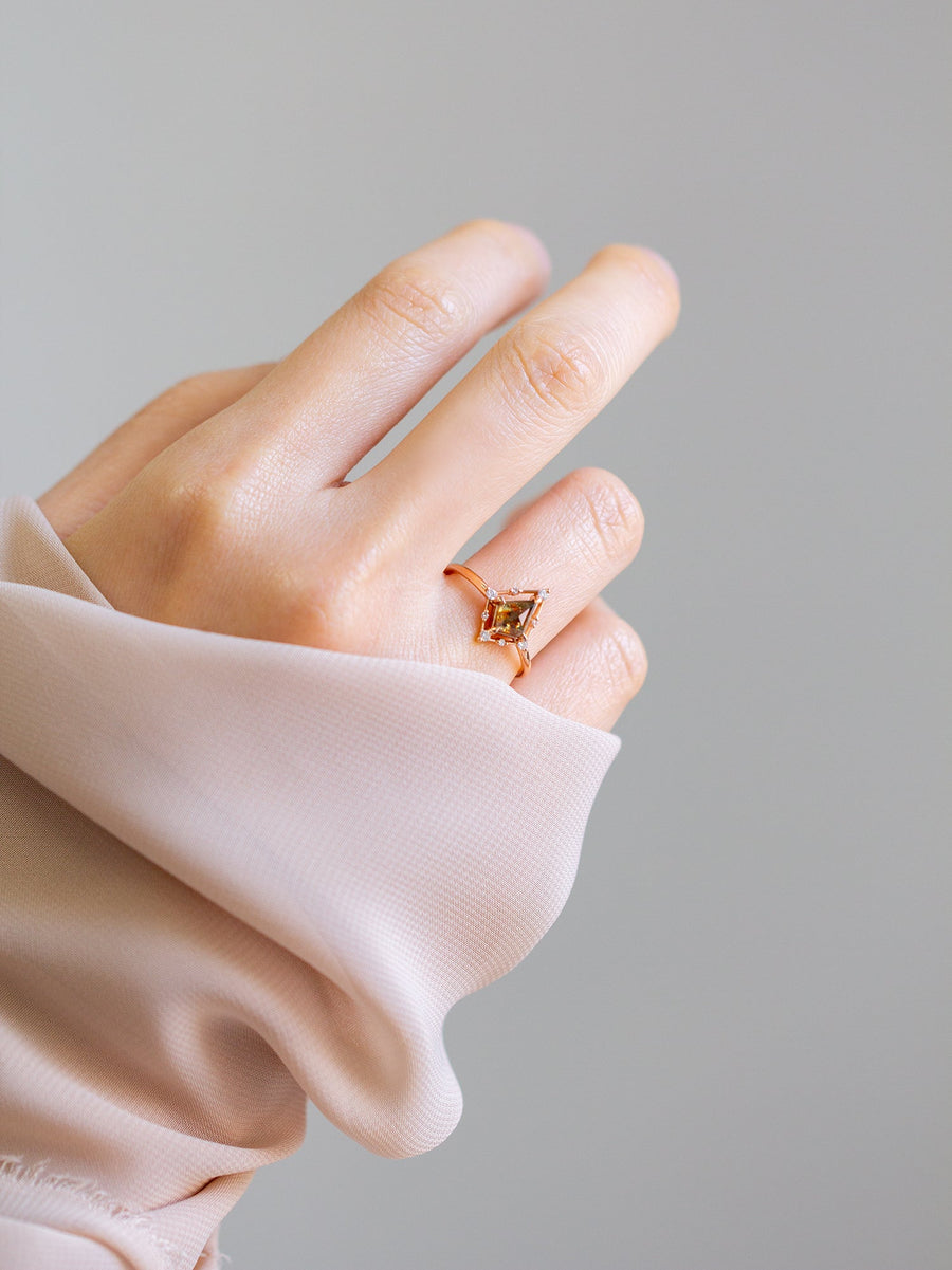 Minimal art deco styled kite shaped salt and pepper diamond engagement ring in 14k rose gold with smaller round diamonds on model's hand.