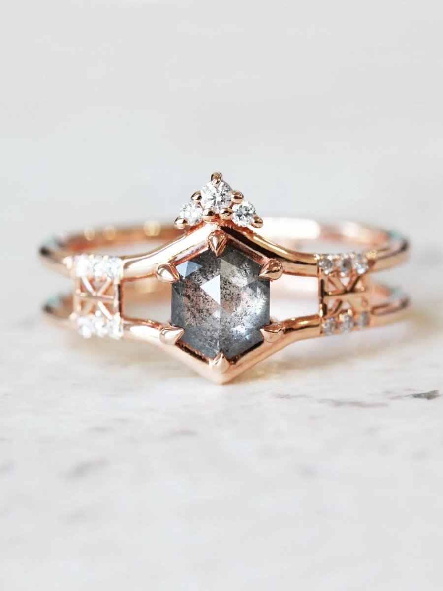 Face of contemporary double-banded chevron engagement ring with hexagon center, round melee trefoil, and Art Deco lattice on marble top