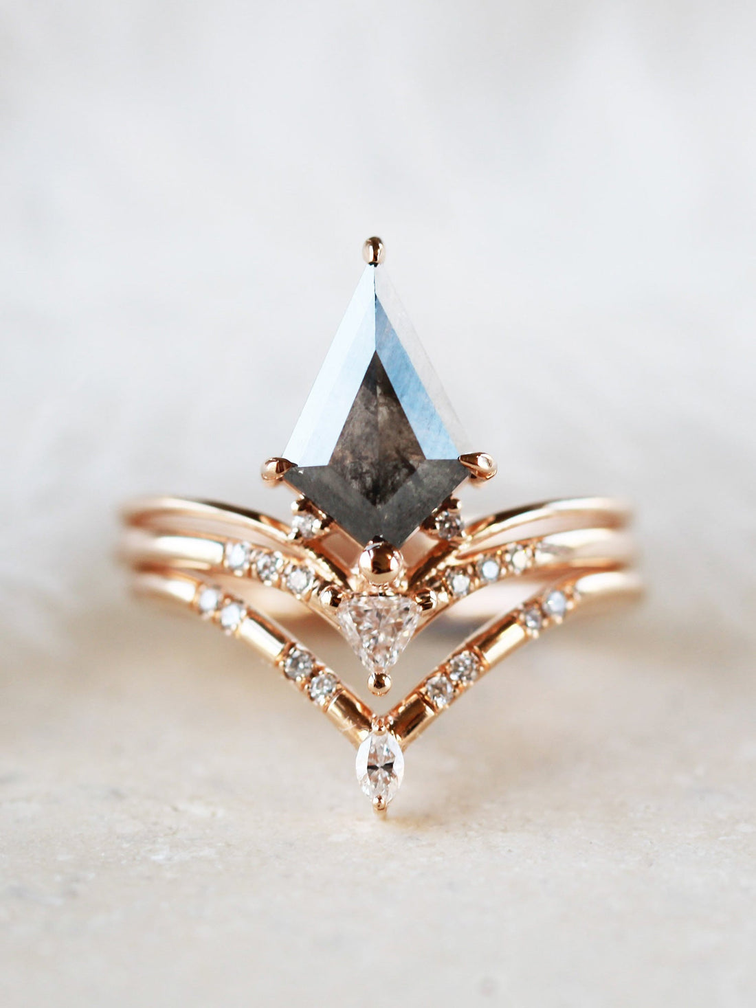Minimalistic and art deco styled kite salt and pepper diamond engagement ring in 14k rose gold with a trilliant and round diamonds with matching band.