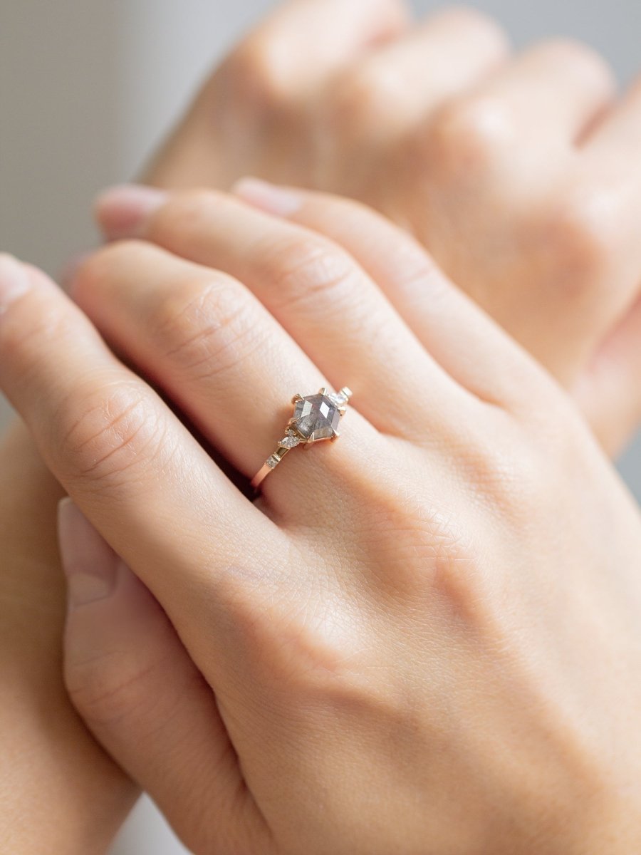 Unique art deco styled hexagon shaped salt and pepper diamond engagement ring in 14k rose gold with smaller marquise, round, and princess cut diamonds on model's hand.