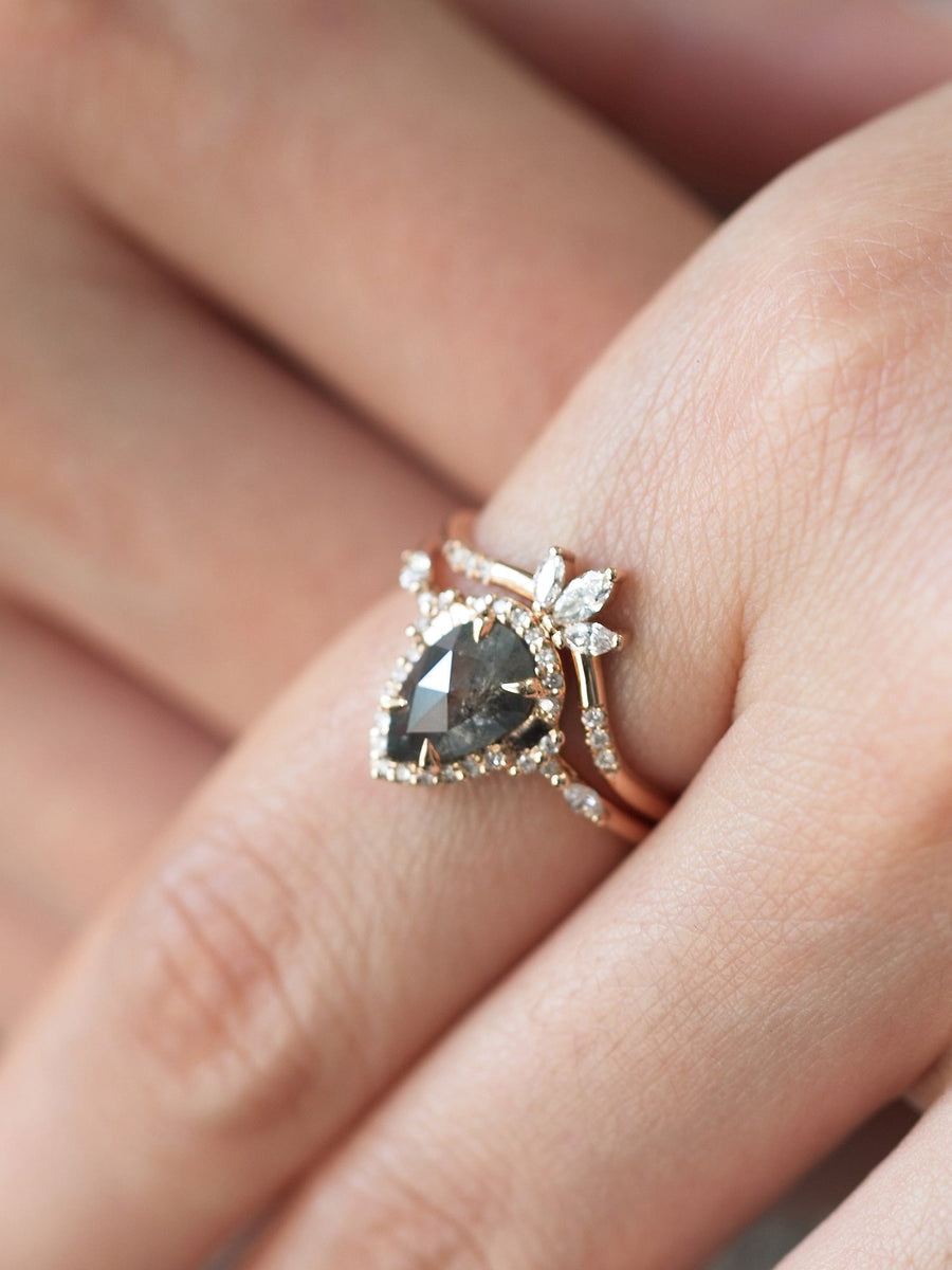 Pear-shaped salt and pepper diamond engagement ring in 14k rose gold  with matching band inspired by the art deco style and minimalism on model's hand.