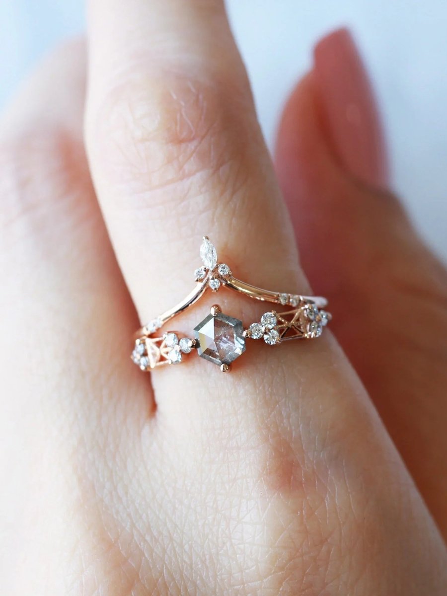Close-up of a finger wearing a Modern Art Deco engagement ring with a salt and pepper hexagon diamond center, round trefoil clusters, and architectural latticework, stacked under a chevron band