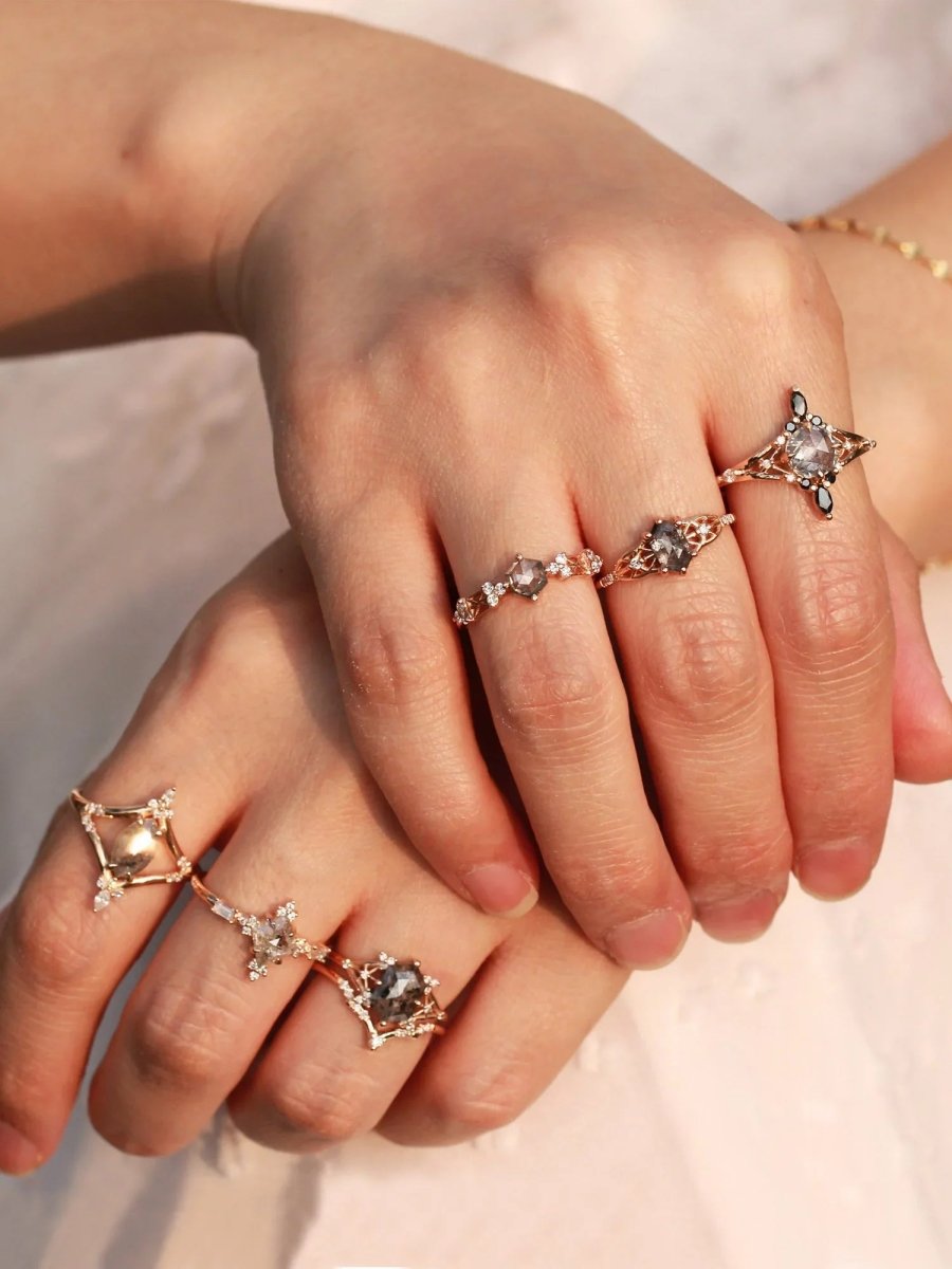 Two hands resting on each other, wearing a series of Modern Art Deco architectural-inspired rings with salt and pepper diamonds
