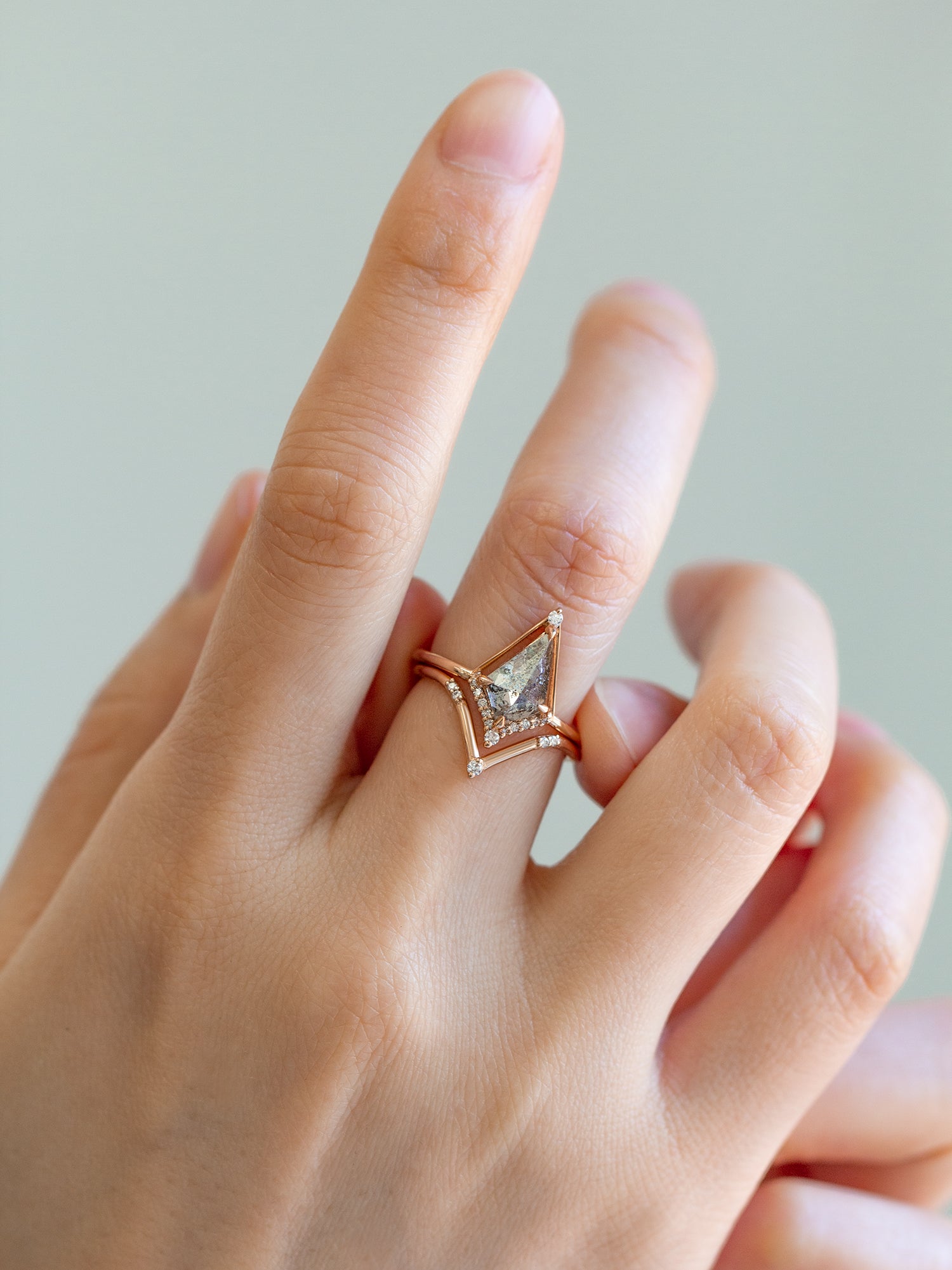 Kite shape salt and pepper diamond engagement ring with smaller round diamonds in 14k gold inspired by the art deco style and minimalism on model’s hand.