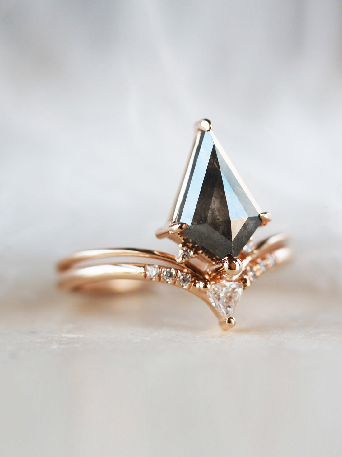 Minimalistic and art deco styled kite salt and pepper diamond engagement ring in 14k rose gold with a trilliant and round diamonds.